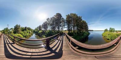 full seamless panorama 360 by 180 angle view on wooden bridge across water canal against backdrop of huge lake in sunny summer day in equirectangular projection, skybox VR virtual reality content photo