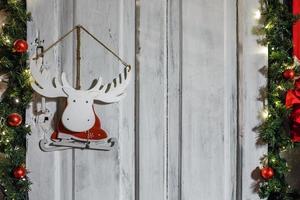 patines de alces de juguete de madera en un traje de santa claus colgado en una pared rodeada de ramas de abeto foto