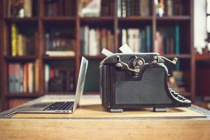 old vintage dust-covered typewriter with sheet of white paper near modern notebook on bookcase background. modern technology and vintage appliances photo