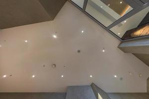 look up on suspended ceiling with halogen spots lamps and drywall construction with fire alarm sensor in empty room in apartment or house. Stretch ceiling white and complex shape. photo