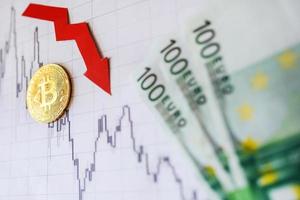 Depreciation of virtual money bitcoin. Red arrow and golden Bitcoin on paper forex chart index rating go down exchange market background with euro banknotes. Concept depreciation of cryptocurrency. photo