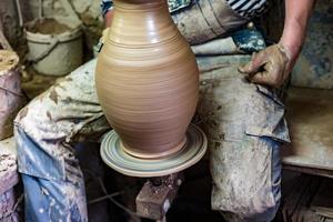 Craftsman in dirty clothes molding clay into desired shape on potter's wheel. photo