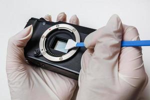 Close-up of mirrorless digital APS-C dirty camera matrix sensor cleaning and maintenance with swab, photographer cleaning photocamera on white background photo