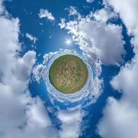 tiny planet in blue sky with beautiful curly clouds. Transformation of spherical panorama 360 degrees. Spherical abstract aerial view. Curvature of space. photo