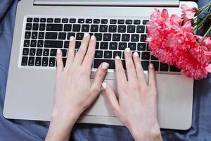 Hands, computer keyboard, bed top view. Workplace background, work at home, notepad and flowers photo