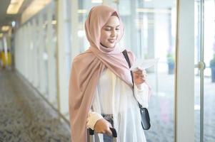 Young female muslim traveler carrying suitcases at the International airport, travel, holidays and journey concept. photo