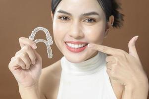 A young woman with beautiful teeth is holding Invisalign, healthy dental concept photo