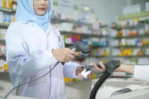 Farmacéutico musulmán femenino escaneando código de barras en una farmacia moderna. foto