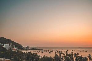 vista aérea de la ciudad de vung tau con hermosa puesta de sol y tantos barcos. vista panorámica costera de vung tau desde arriba, con olas, costa, calles, cocoteros y montaña tao phung en vietnam. foto