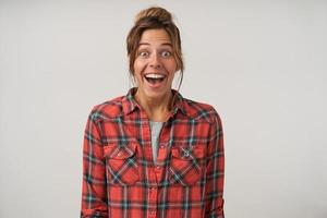 foto de estudio de una mujer joven y sorprendida con pantalones a cuadros, sonriendo ampliamente a la cámara con peinado casual y maquillaje natural, aislada sobre fondo blanco