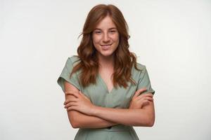 Indoor portrait of pretty curly female with curls standing over white backgroung with crossed arms, looking to camera and smiling joyfully photo