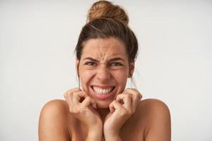 Young beautiful woman posing over white background with frightened face, scaredly holding hands by face, grimacing and showing teeth photo