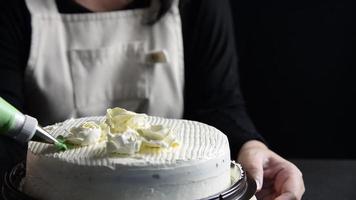 Köchin, die Rosen aus Sahne für die Dekoration von Kuchen herstellt, während sie hausgemachte Backwaren von oben auf schwarzem Hintergrund macht video