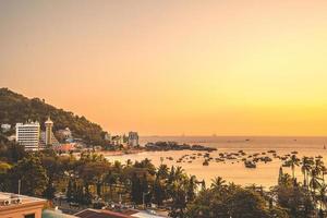 Vung Tau city aerial view with beautiful sunset and so many boats. Panoramic coastal Vung Tau view from above, with waves, coastline, streets, coconut trees and Tao Phung mountain in Vietnam. photo