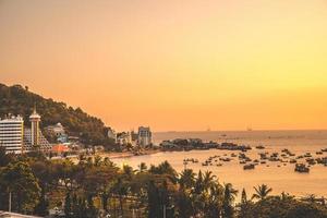 Vung Tau city aerial view with beautiful sunset and so many boats. Panoramic coastal Vung Tau view from above, with waves, coastline, streets, coconut trees and Tao Phung mountain in Vietnam. photo