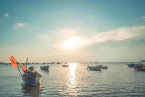 paisaje marino tropical con un barco en la playa de arena al amanecer o al atardecer nublado. hermosa playa tropical al atardecer con bote pequeño y cielo cinematográfico para viajes y vacaciones en tiempo de relajación de vacaciones. foto