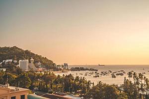 Vung Tau city aerial view with beautiful sunset and so many boats. Panoramic coastal Vung Tau view from above, with waves, coastline, streets, coconut trees and Tao Phung mountain in Vietnam. photo