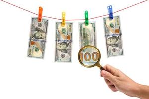 Dollars are suspended by clothespins on white background and examined with a magnifying glass.