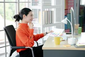 Female director working in office sitting at desk analyzing business statistics holding diagrams and charts using computer photo