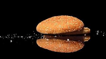 pan de hamburguesa cayendo sobre espejo negro en cámara lenta. aislado sobre fondo negro video