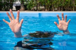 Woman showing her hands while drowing in swimming pool. Drowning is the process of experiencing respiratory impairment from submersion or immersion in liquid. photo