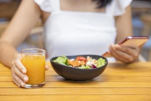 Woman eating Breakfast and play smart phone. Fruits such as watermelon, papaya, melon, passion fruit, orange juice and coffee. placed on a gray placemat photo