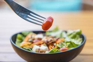 use un tenedor, una brocheta de tomate en primer plano y una ensalada en el fondo. ensalada de desayuno con verduras salteadas en una mesa de madera foto