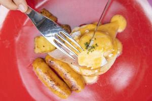 Woman's hand holding a fork and eating Breakfast. Egg Benedict, fruits such as watermelon, papaya, melon, passion fruit, orange juice and coffee. placed on a gray placemat photo