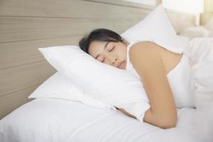 joven asiática durmiendo en la cama en el dormitorio. ella está acostada de lado y se relaja con los ojos cerrados foto