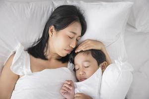 joven asiática e hijo durmiendo en su cama y relajándose en el dormitorio. están acostados de lado y se relajan con los ojos cerrados foto