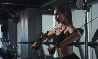 Sporty woman exercising on multistation at gym for arm and shoulders muscles. Fitness exercising in gym. photo