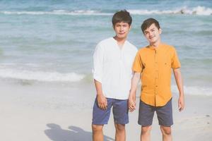 Homosexual portrait young asian couple standing together on beach in summer, asia gay holding hands going sea for leisure and relax with romantic and happy in vacation at sea, LGBT with legal concept. photo