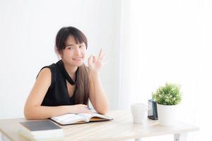 hermoso retrato joven mujer asiática sonriendo sentada estudiando y aprendiendo a escribir cuaderno y diario en la sala de estar en casa, tarea de niña, mujer de negocios trabajando en la mesa, concepto de educación. foto