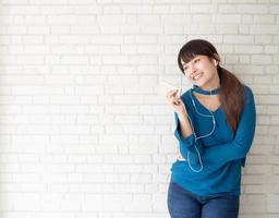 hermoso retrato mujer joven asiática de pie feliz disfrutar y divertirse escuchar música con auriculares sobre fondo de hormigón de cemento, estilo de vida de chica relajar radio de sonido con auriculares, concepto de tecnología. foto