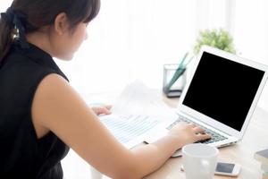 Young asian woman working and typing with laptop computer at office, businesswoman looking graph diagram analysis statistic data of finance, girl using notebook, profit growth, business concept. photo
