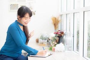 Beautiful portrait asian woman writer excited writing on notebook or diary with happy with success and glad, lifestyle asia girl is student, female plan working, education and business concept. photo