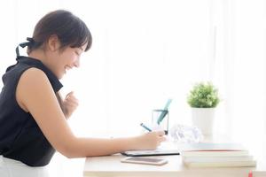 hermosa joven escritora asiática emocionada escribiendo en un cuaderno o diario feliz con éxito y contenta, estilo de vida chica asiática es estudiante, planificación femenina trabajo, educación y concepto de negocios. foto