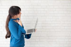 Beautiful asian young woman hipster using working laptop thinking idea on cement concrete background, girl doubt and question with computer internet online, freelance and business concept. photo