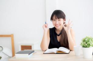 Beautiful portrait young asian woman smiling sitting study and learning writing notebook and diary in the living room at home, girl homework, business woman working on table, education concept. photo