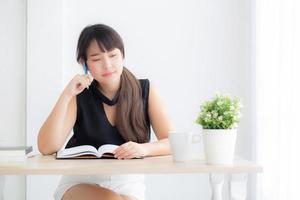 Young asian woman writer smiling thinking idea and writing on notebook or diary with happy on desk office, lifestyle of asia girl is success, female planning working, education and business concept. photo