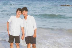 retrato homosexual joven pareja asiática de pie juntos en la playa en verano, asia gay tomados de la mano yendo al mar por placer y relajarse con romántico y feliz en vacaciones en el mar, lgbt con concepto legal. foto