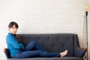 Beautiful portrait young asian woman sitting and smiling happy and looking at camera on sofa with casual at living room, girl cheerful and relax on couch at home, lifestyle concept. photo