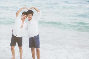 retrato homosexual joven pareja asiática stand gesto forma de corazón juntos en la playa en verano, abrazo gay de asia y yendo al mar por placer con romántico y feliz en vacaciones, lgbt con concepto legal. foto