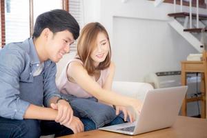 Asian young couple using laptop computer think and searching internet together, man and woman casual smiling work at home with happy and relax, communication and business concept. photo