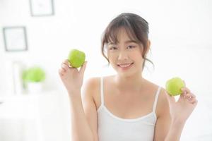 hermoso retrato joven mujer asiática sosteniendo y comiendo fruta de manzana verde en el dormitorio en casa, estilo de vida de nutrición niña saludable y cuidado concepto de pérdida de peso, salud y bienestar. foto