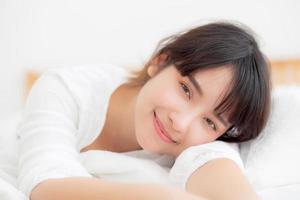 hermoso retrato joven mujer asiática acostada y sonriendo mientras se despierta con el amanecer en la mañana, chica feliz y divertida en el dormitorio, estilo de vida y concepto de relajación. foto