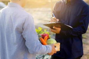 Two young asian man checking and picking up organic fresh vegetable in hydroponic farm and writing record document grow of leaf for quality produce, small business owner concept. photo