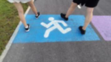 blurred picture of close up white painting walking sign or icon on blue background with people are walking for exercise in public park.Bangkok Thailand photo