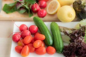 vista superior de los tomates cherry se colocan en una bandeja con rábanos, pepinos, lechuga de roble rojo y otras frutas y verduras. como materia prima para hacer ensaladas en la mesa de la cocina. foto