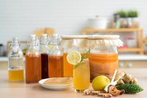 Kombu tea in a glass with ice, lemon slices and rosemary leaves, Homemade fermented raw kombucha tea in glass and bottles mix with fruit juice, scoby and herb on table.Healthy natural probiotic drink. photo